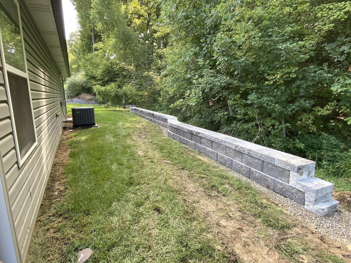 A long block retaining wall with a stepped end, built along a mown lawn beside a house