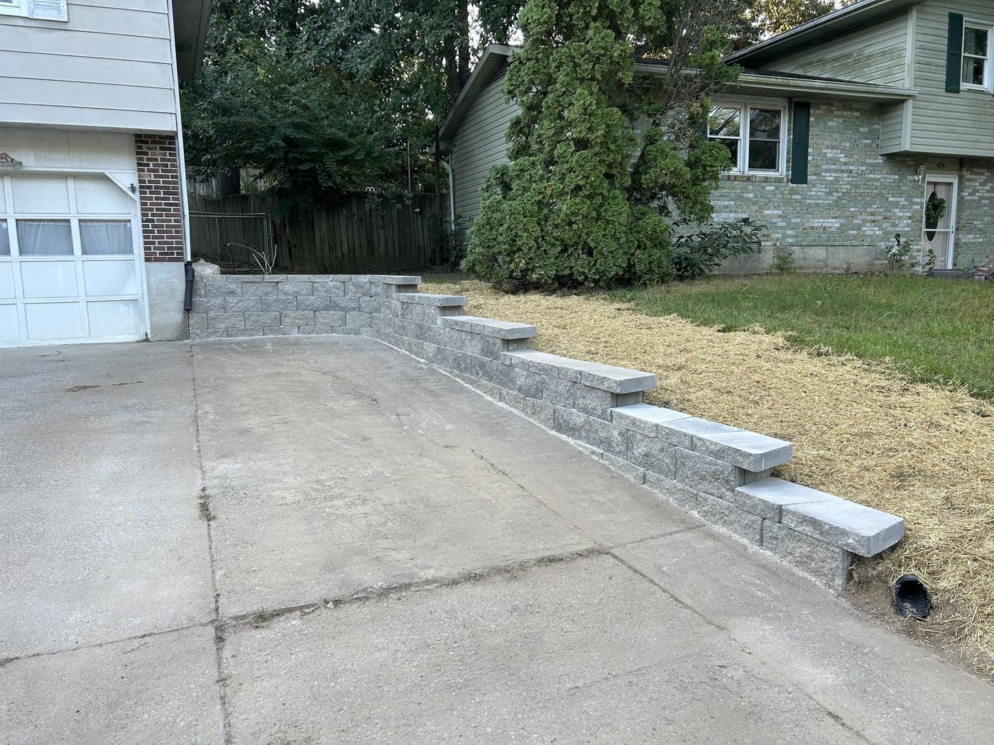 A block retaining wall with wide stepped treads running beside a driveway